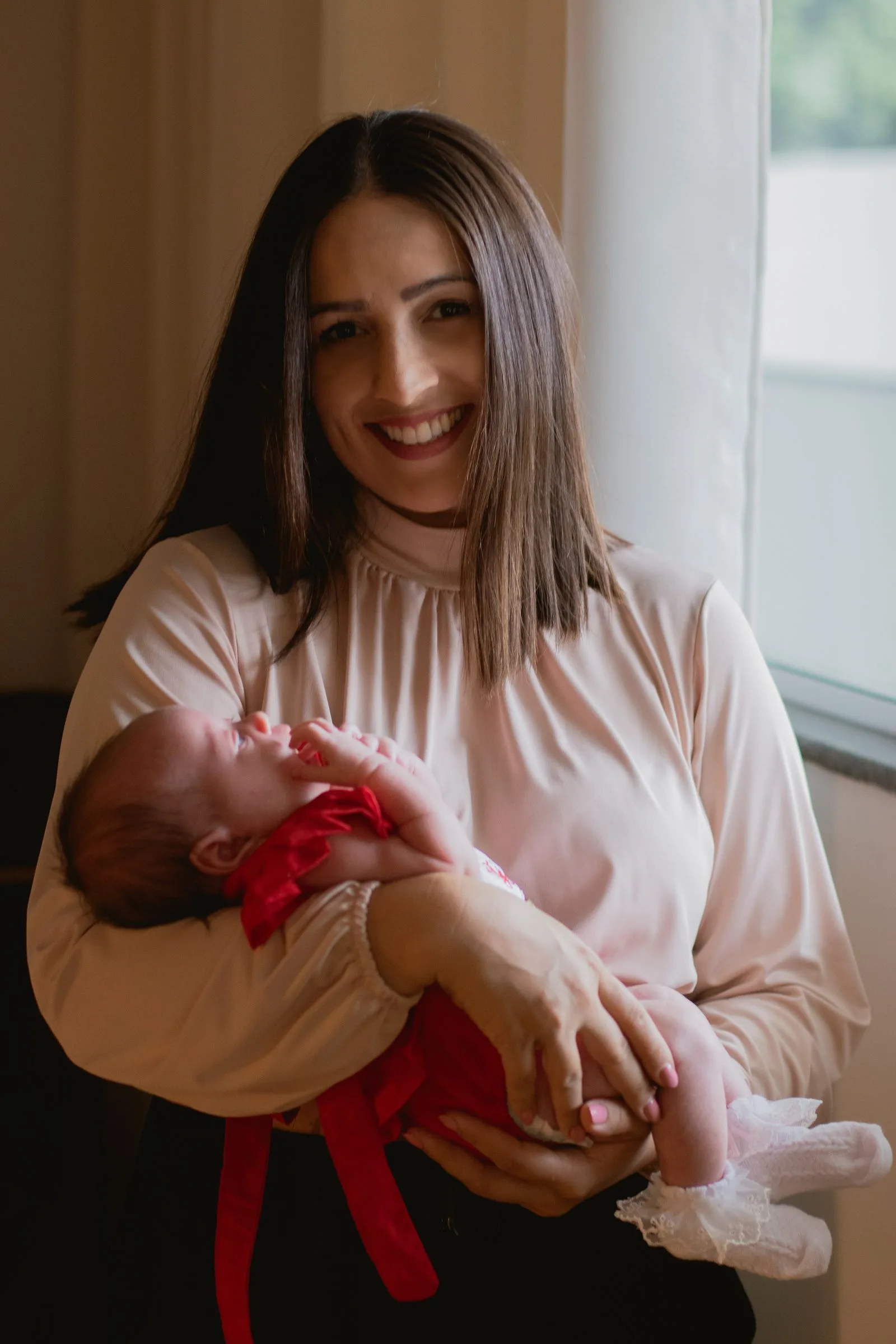 Mother smiling while holding her newborn baby in soft window light